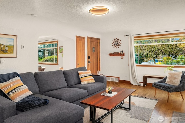 living area featuring baseboards, visible vents, wood-type flooring, and a textured ceiling