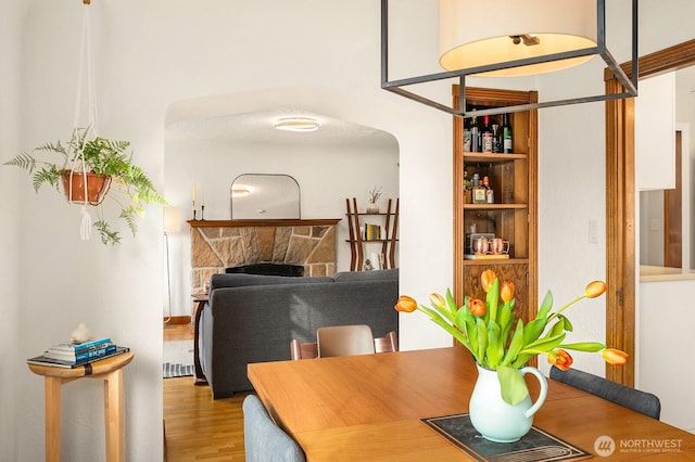 dining area featuring arched walkways, a fireplace, and wood finished floors