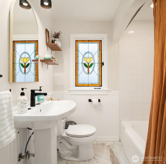 full bathroom featuring a wealth of natural light, a wainscoted wall, marble finish floor, and toilet