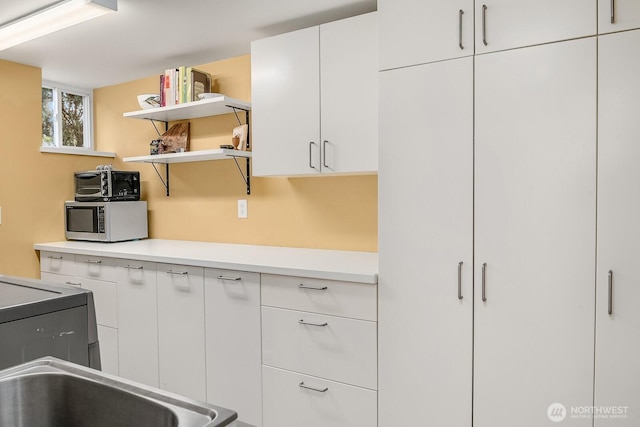 kitchen featuring open shelves, stainless steel microwave, white cabinetry, a toaster, and light countertops