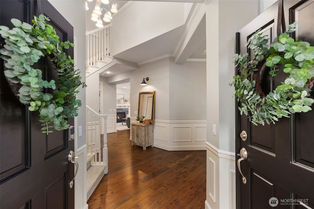 entryway featuring dark wood-type flooring, stairway, a wainscoted wall, ornamental molding, and a decorative wall