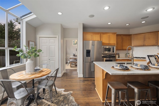 kitchen featuring dark wood finished floors, recessed lighting, appliances with stainless steel finishes, a kitchen breakfast bar, and backsplash