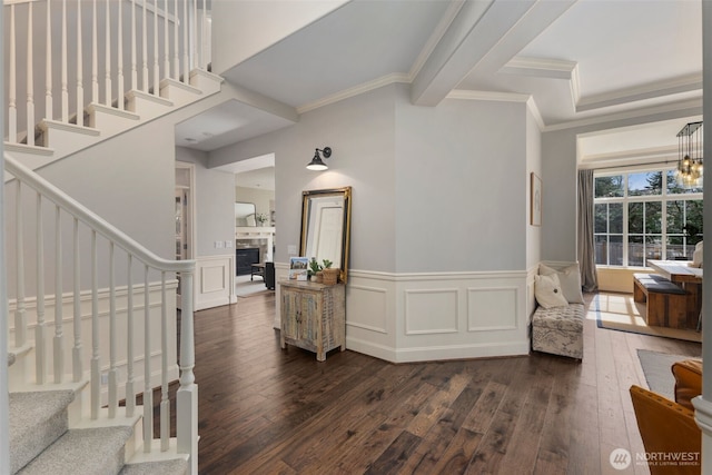 entryway with stairs, wainscoting, a fireplace, crown molding, and dark wood-style flooring