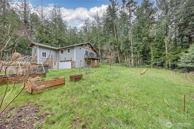 view of yard featuring a garden, a wooden deck, a wooded view, and an attached garage