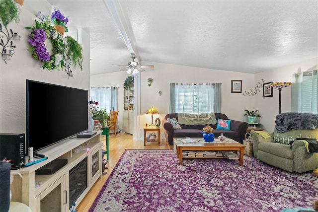 living area with lofted ceiling with beams, light wood-type flooring, a textured ceiling, and a ceiling fan