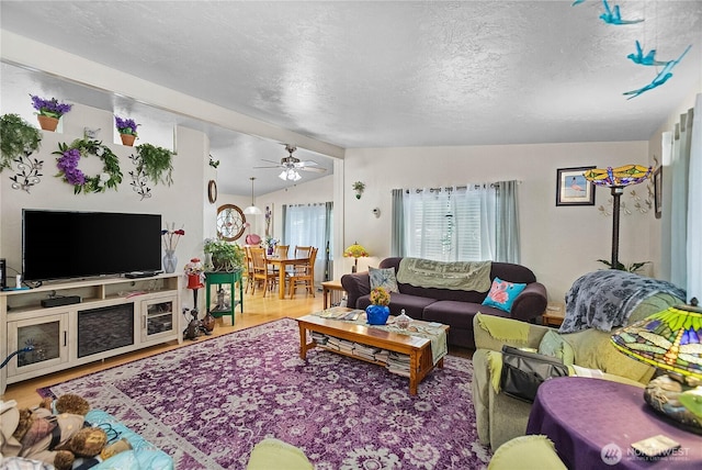 living area with ceiling fan, lofted ceiling, wood finished floors, and a textured ceiling