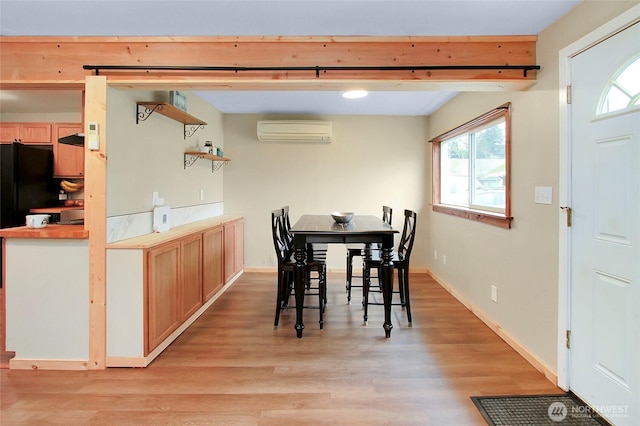 dining room with an AC wall unit, light wood-type flooring, and baseboards