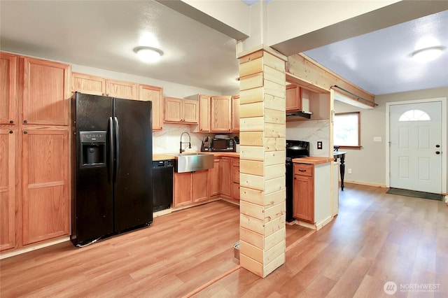 kitchen with light wood finished floors, black appliances, light countertops, and a sink