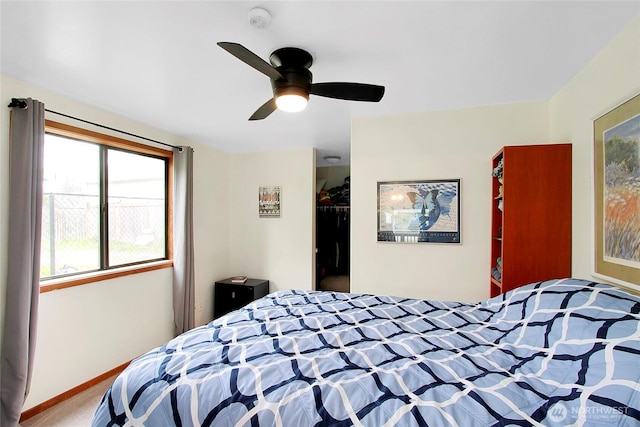 carpeted bedroom with a closet, baseboards, a walk in closet, and a ceiling fan