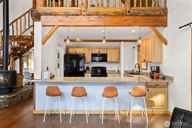 kitchen featuring light brown cabinetry, light stone counters, a wood stove, black appliances, and a sink