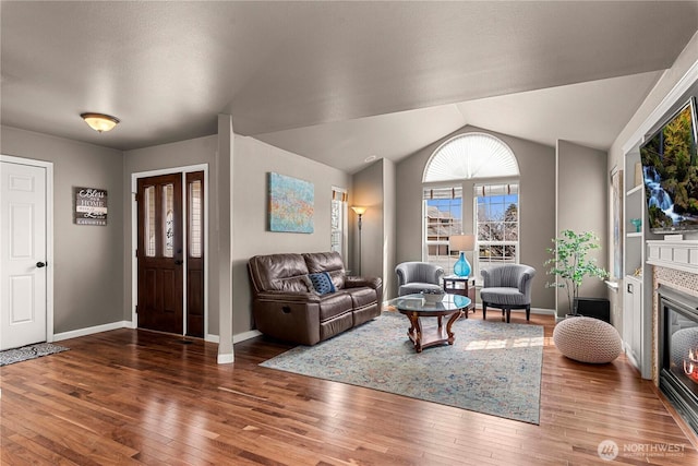 living area with hardwood / wood-style flooring, a fireplace, baseboards, and vaulted ceiling