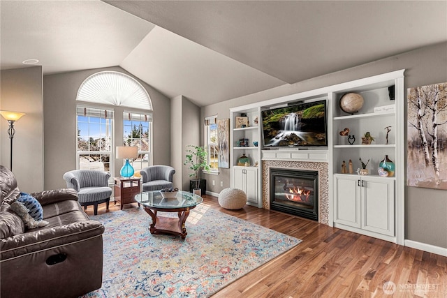 living area featuring vaulted ceiling, wood finished floors, baseboards, and a tile fireplace