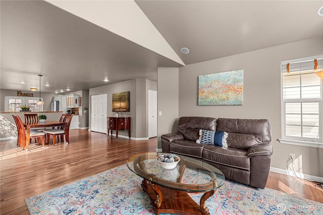 living area with baseboards, lofted ceiling, and wood finished floors