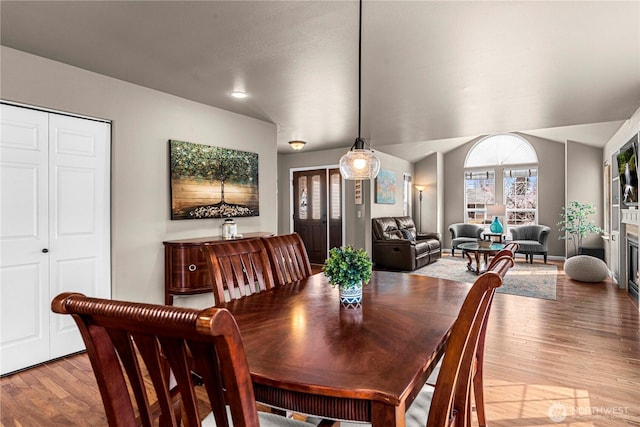 dining area featuring wood finished floors, a glass covered fireplace, and vaulted ceiling