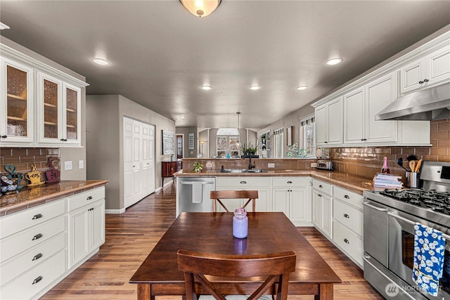 kitchen featuring a sink, wood finished floors, stainless steel appliances, a peninsula, and white cabinets