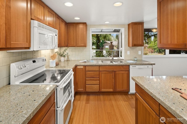 kitchen with light wood-style flooring, a sink, white appliances, brown cabinetry, and light stone countertops