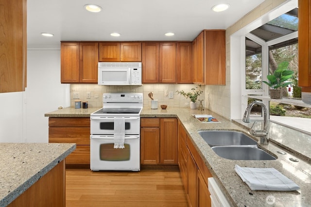 kitchen with brown cabinetry, white appliances, light stone counters, and a sink