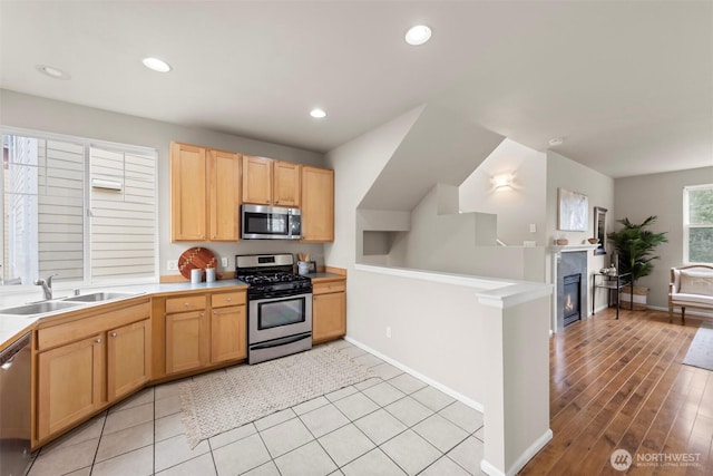 kitchen featuring a sink, a glass covered fireplace, recessed lighting, stainless steel appliances, and light countertops