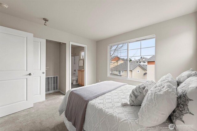 bedroom with visible vents, ensuite bathroom, and carpet flooring