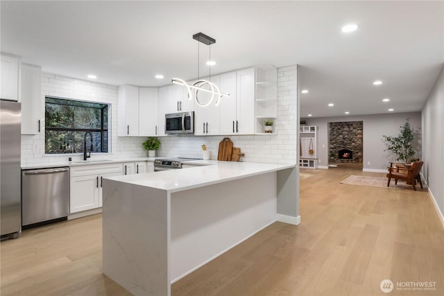 kitchen with a sink, light wood-style flooring, white cabinets, stainless steel appliances, and open shelves