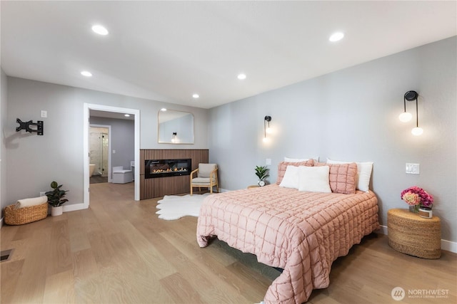 bedroom with a glass covered fireplace, recessed lighting, light wood-type flooring, and baseboards