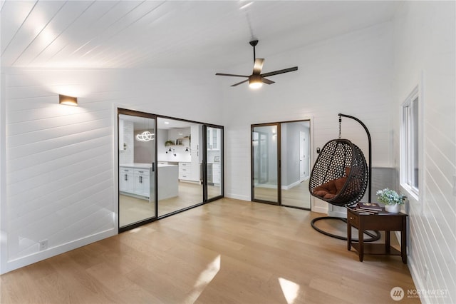 living area featuring light wood-style flooring, baseboards, ceiling fan, and a towering ceiling