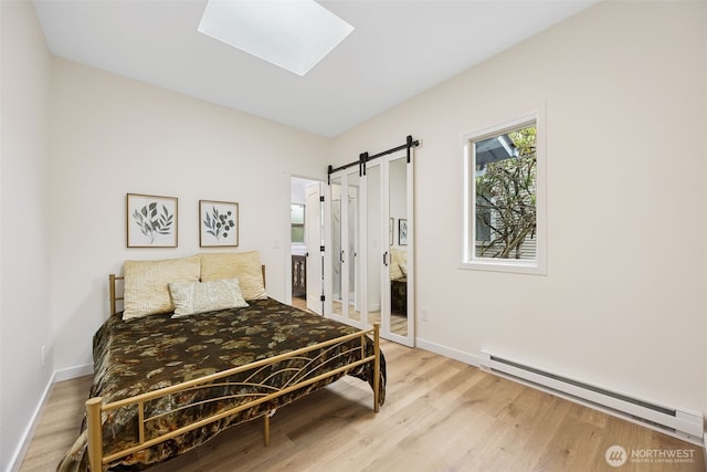 bedroom with a barn door, wood finished floors, baseboard heating, and a skylight