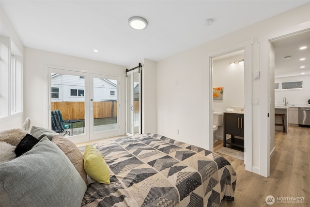 bedroom featuring light wood-style flooring, access to outside, recessed lighting, a barn door, and connected bathroom