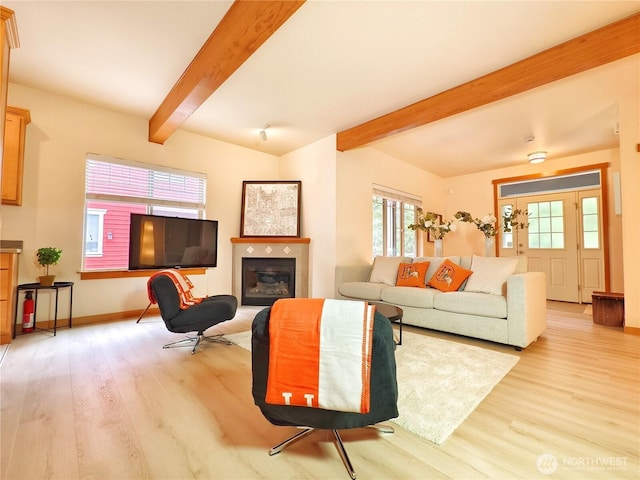 living room featuring a fireplace, beamed ceiling, light wood-style flooring, and baseboards