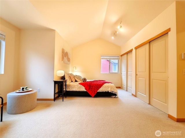 carpeted bedroom with baseboards, lofted ceiling, and multiple closets