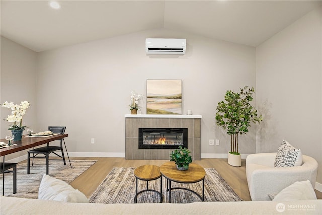 living area featuring a wall unit AC, wood finished floors, baseboards, a fireplace, and vaulted ceiling