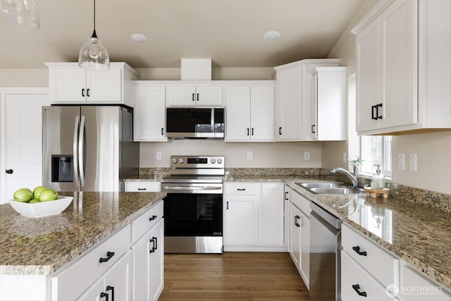 kitchen with pendant lighting, appliances with stainless steel finishes, wood finished floors, white cabinets, and a sink