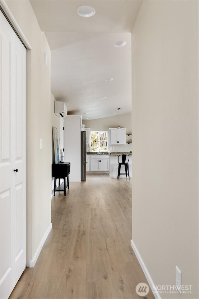 corridor featuring light wood-style flooring, baseboards, and a wall unit AC