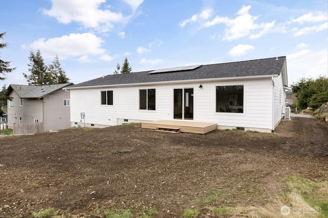 rear view of property with a deck, a shingled roof, roof mounted solar panels, and crawl space