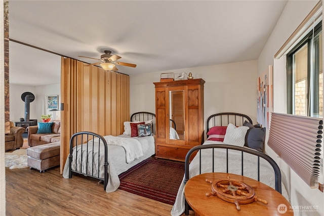 bedroom with ceiling fan, wood finished floors, and a wood stove