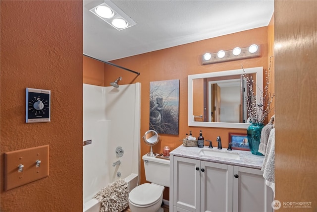 bathroom with toilet, vanity, shower / bathing tub combination, and a textured wall