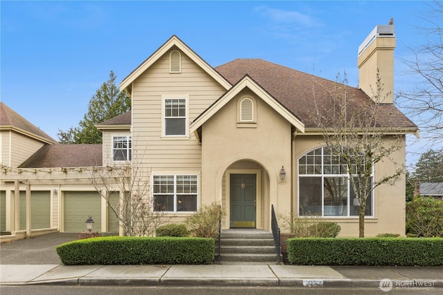 traditional-style house featuring roof with shingles, driveway, an attached garage, stucco siding, and a chimney