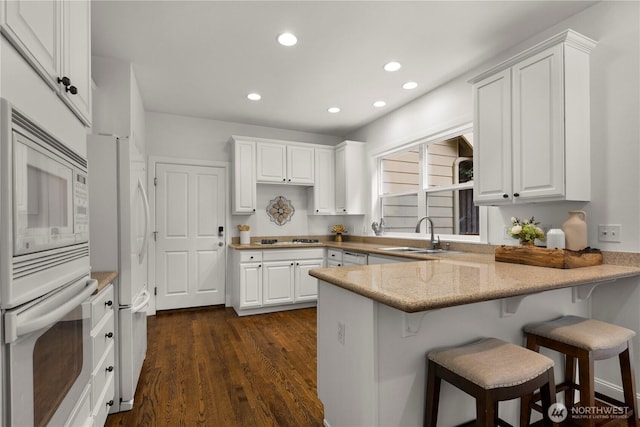 kitchen with white appliances, white cabinetry, a peninsula, and a sink