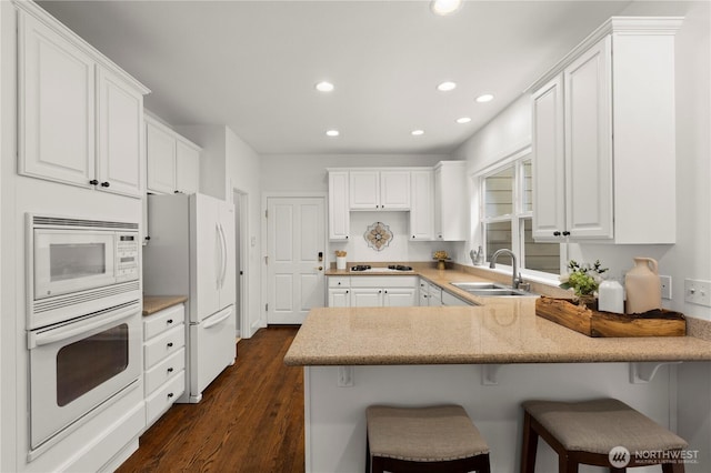 kitchen with recessed lighting, a peninsula, white appliances, white cabinetry, and a sink