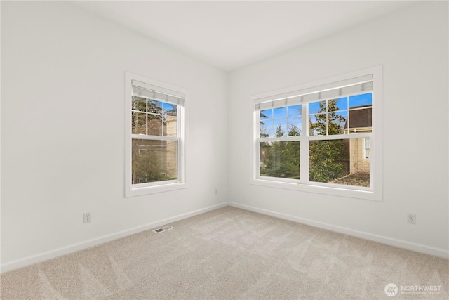 carpeted spare room with baseboards, visible vents, and a wealth of natural light