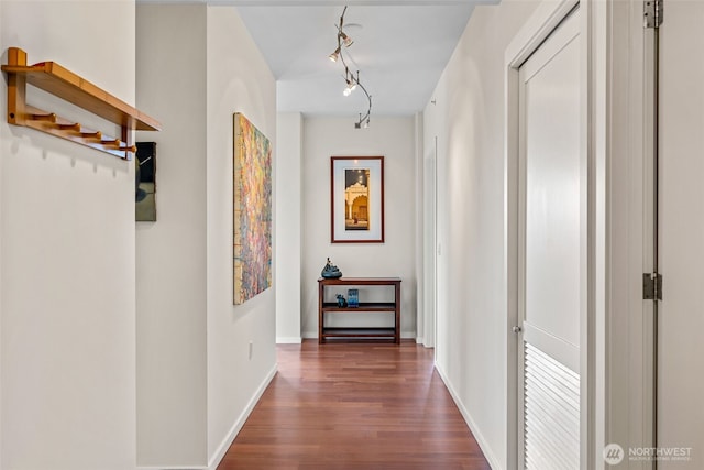 hall featuring dark wood-style flooring, baseboards, and rail lighting