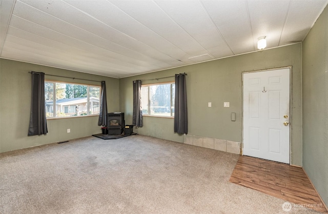 unfurnished living room with a wood stove, visible vents, and carpet floors