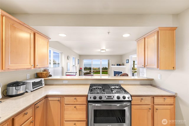 kitchen featuring light brown cabinets, gas range, a peninsula, and light countertops