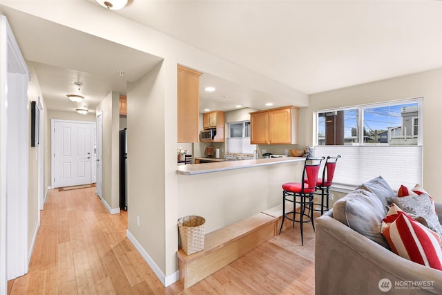 kitchen featuring light brown cabinets, baseboards, light wood-type flooring, appliances with stainless steel finishes, and open floor plan