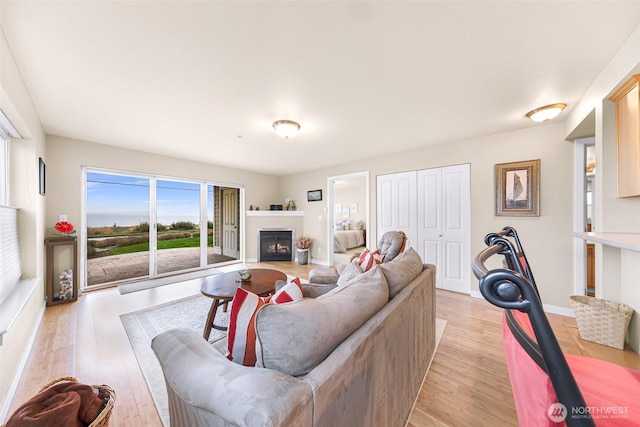 living room featuring light wood finished floors, baseboards, and a warm lit fireplace