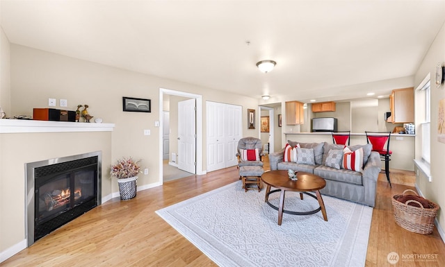 living area featuring light wood finished floors, a glass covered fireplace, and baseboards