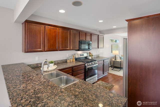 kitchen with stainless steel gas range oven, black microwave, recessed lighting, wood finished floors, and a sink