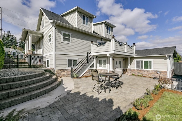 rear view of house featuring a patio, stairway, fence, a shingled roof, and stone siding