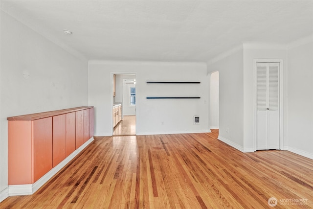 unfurnished room with baseboards, arched walkways, light wood-style floors, and visible vents