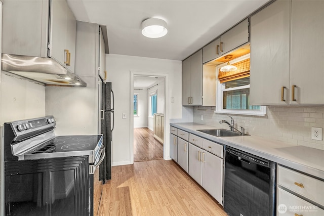 kitchen featuring light wood finished floors, a sink, black appliances, light countertops, and under cabinet range hood